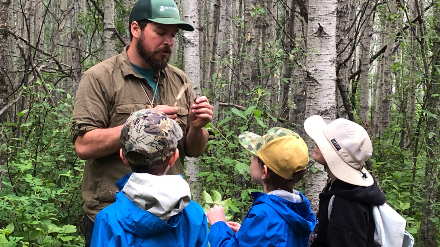 A man standing in a forest instructing three young children